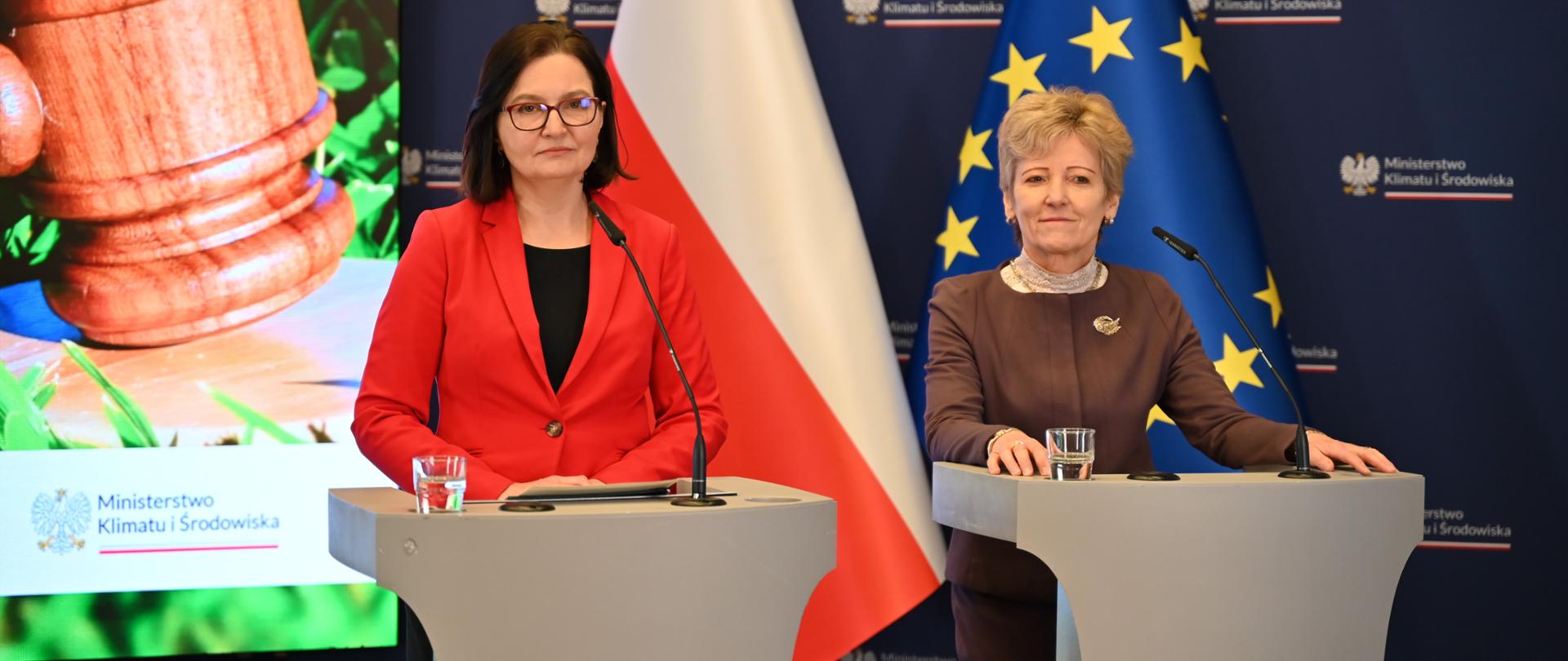 Usprawnienie działania Inspekcji Ochrony Środowiska - konferencja wiceministry klimatu i środowiska Anity Sowińskiej i Głównego Inspektora Ochrony Środowiska Hanny Kończal. Obie kobiety słuchają co ktoś mówi z sali, stoją za mównicami na tle flagi Polski i Unii Europejskiej. Ministra klimatu w czerwonej marynarce, główna inspektor w brązowej marynarce i beżowym golfie. 