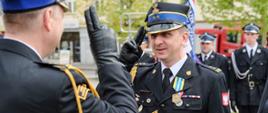 Komendant powiatowy wręcza medal funkcjonariuszowi komendy i oddają sobie honor