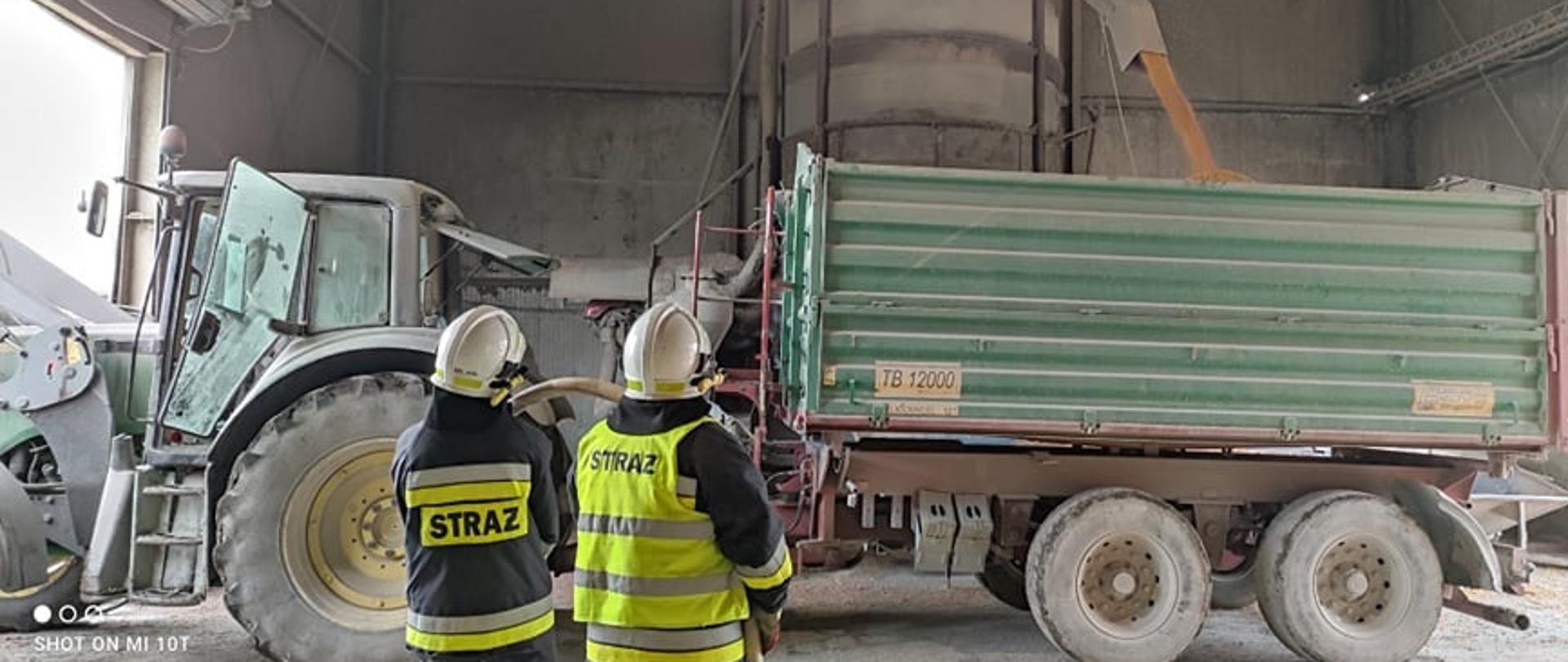 Silos wraz z suszarką zboża z którego opróżniane jest ziarno kukurydzy na podstawiony ciągnik z przyczepą