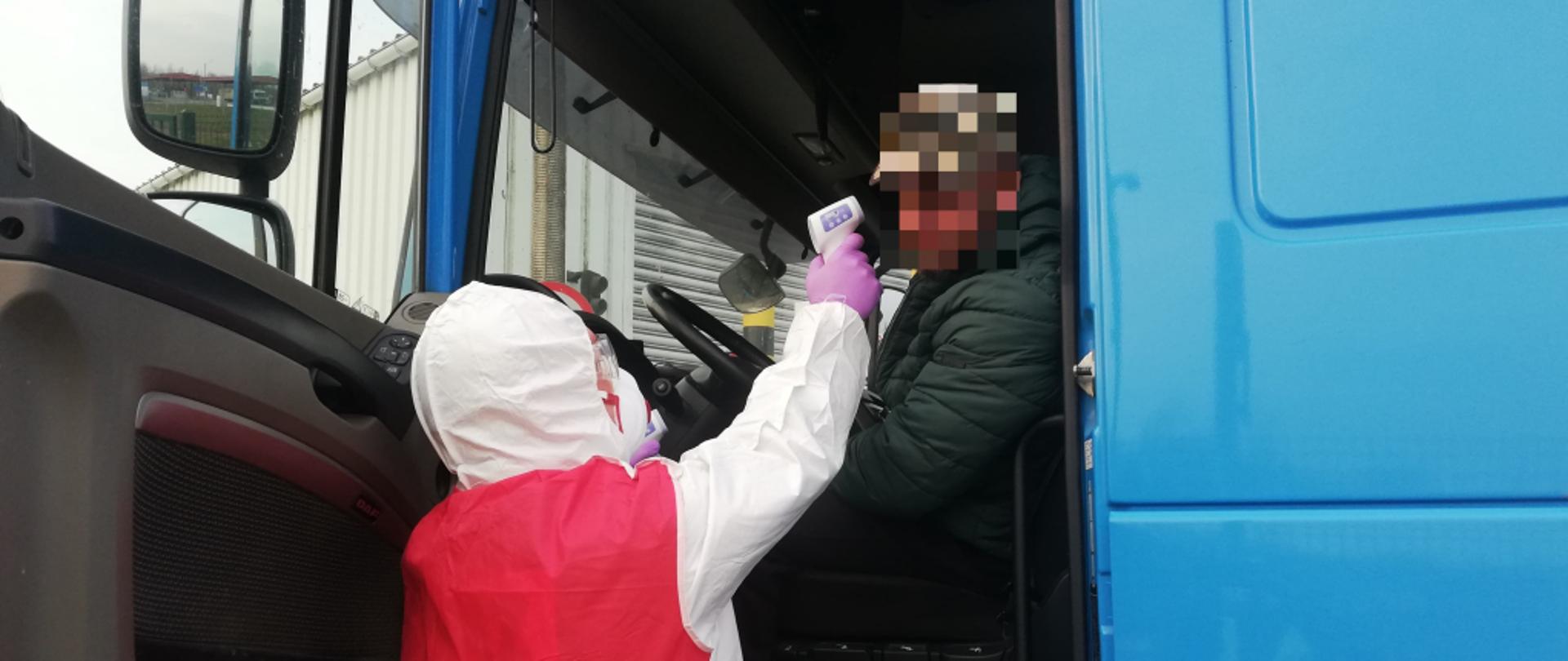 Strażak w specjalnym ubraniu dokonuje pomiaru temperatury kierowcy samochodu ciężarowego