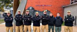 Polska delegacja (8 mężczyzn) pozuje do zdjęcia na tle budynku Chicago Fire Academy