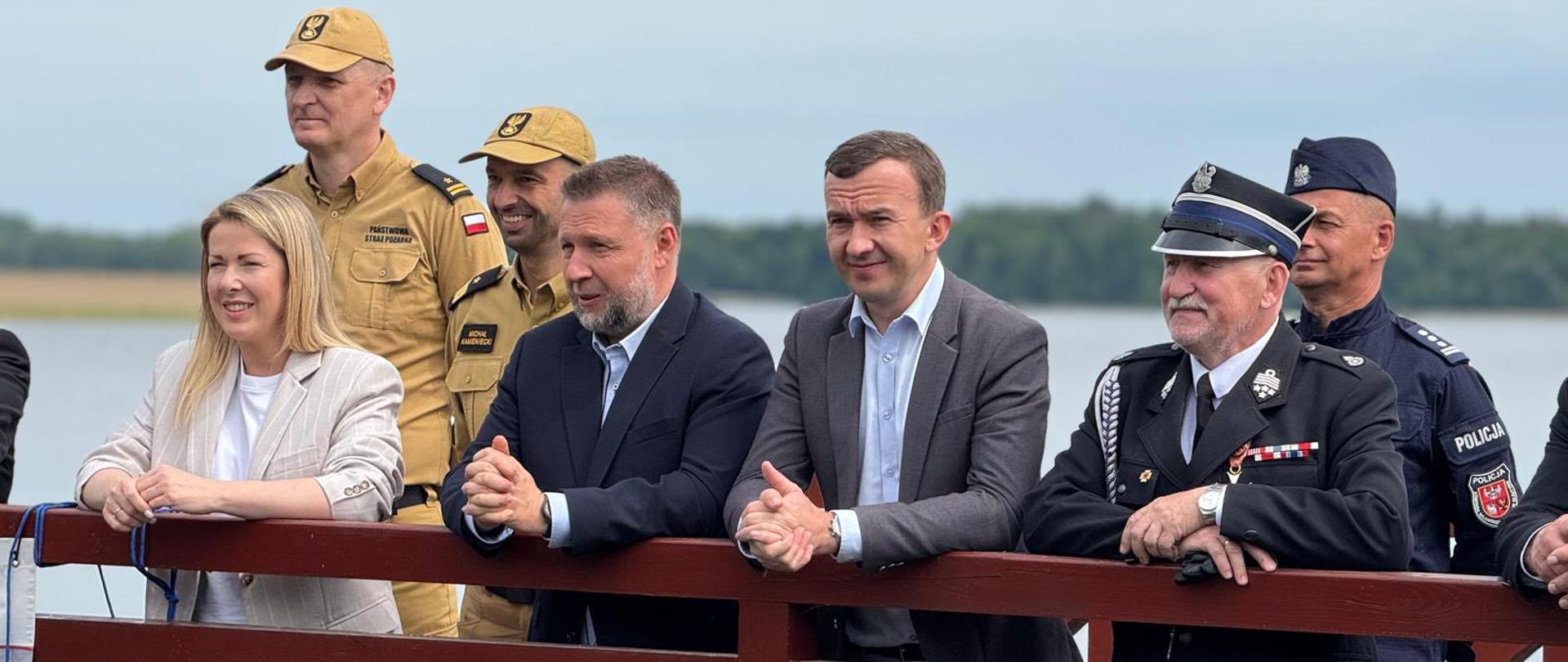Kilkanaście osób stoi na moście i patrzy przed siebie 