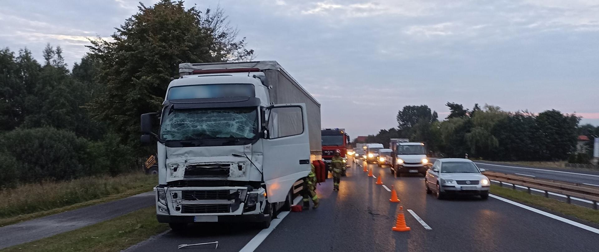Zdjęcie przedstawia samochód ciężarowy po wypadku, obok jadące samochody osobowe