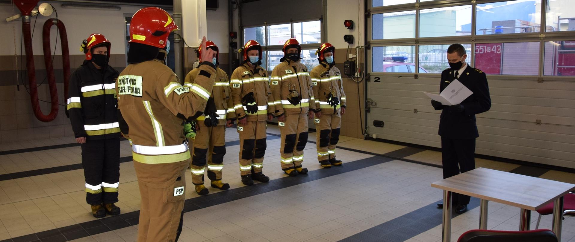 Na zdjęciu po prawej stronie znajduje się zastępca komendanta powiatowego Państwowej Straży Pożarnej w Wąbrzeźnie st.bryg. mgr inż. Ireneusz Wiśniewski odczytujący rotę ślubowania strażakowi Marcinowi Skibskiemu. W tle zmiana służbowa. Zdjęcie zrobione w garażu bojowym, na tle bram garażowych.