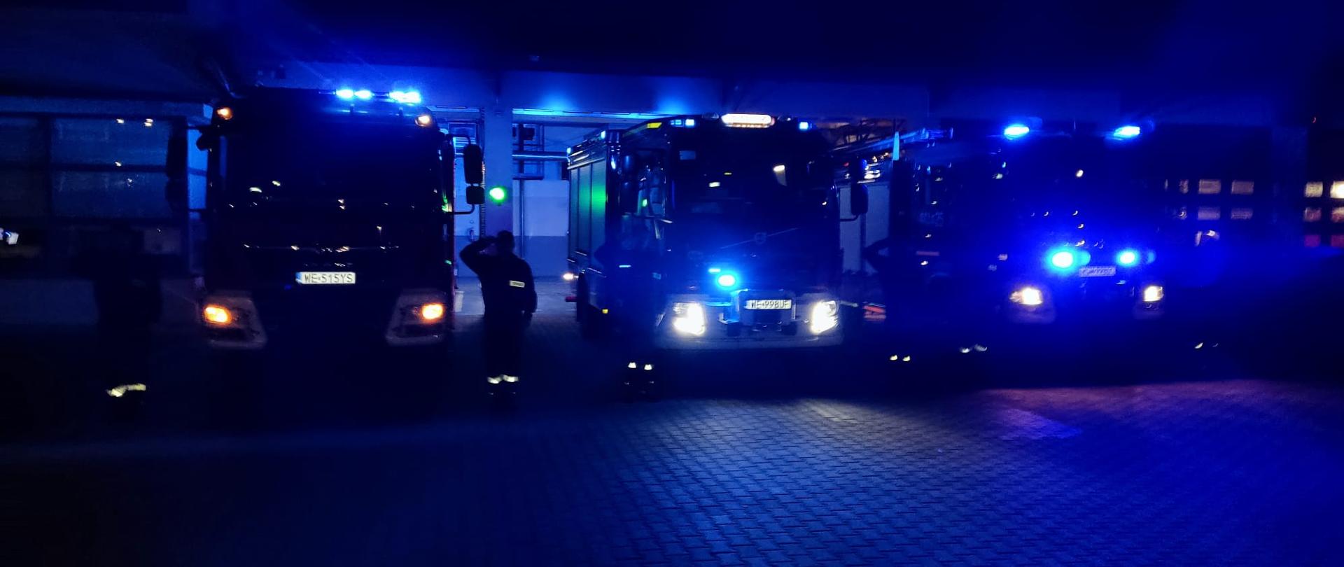 Strażacy stoją przy samochodach pożarniczych, które maja włączone światła błyskowe i sygnały dźwiękowe w celu oddania hołdu śp. sekc. Bartoszowi Błyskala, strażakowi - nurkowi SGRW-N KM PSP Gdańsk, który zmarł w skutek wypadku podczas prowadzonych działań