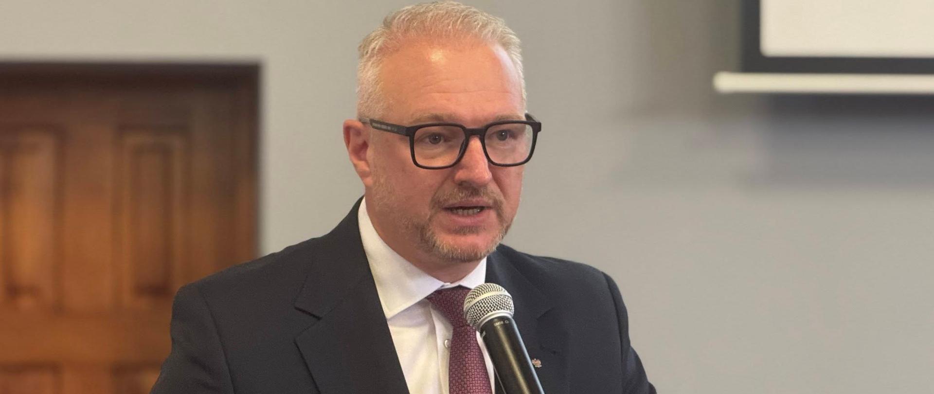 Mężczyzna w garniturze, wojewoda, stoi przy mównicy, przemawia