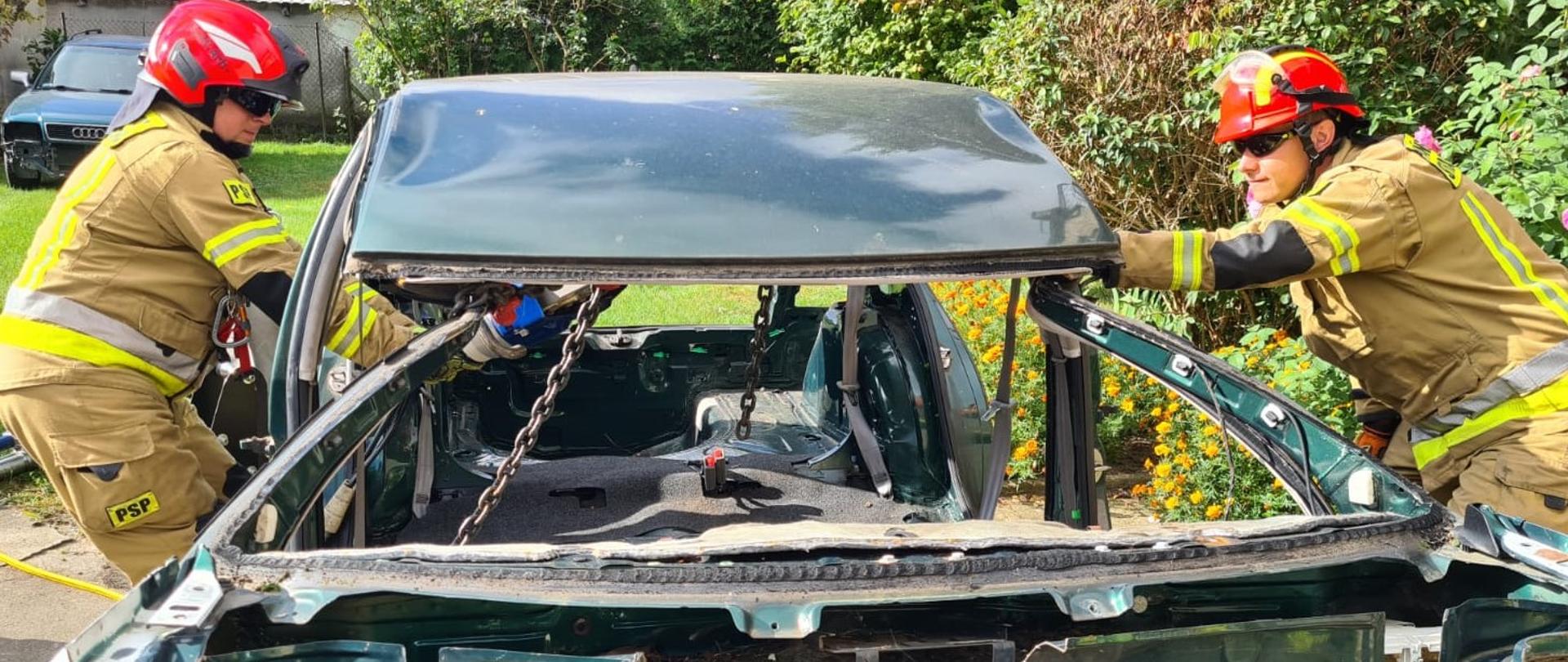 Zdjęcie przedstawia strażaków podczas ćwiczeń doskonalących ze sprzętem ratowniczym.
W tle plac i samochody strażackie.
