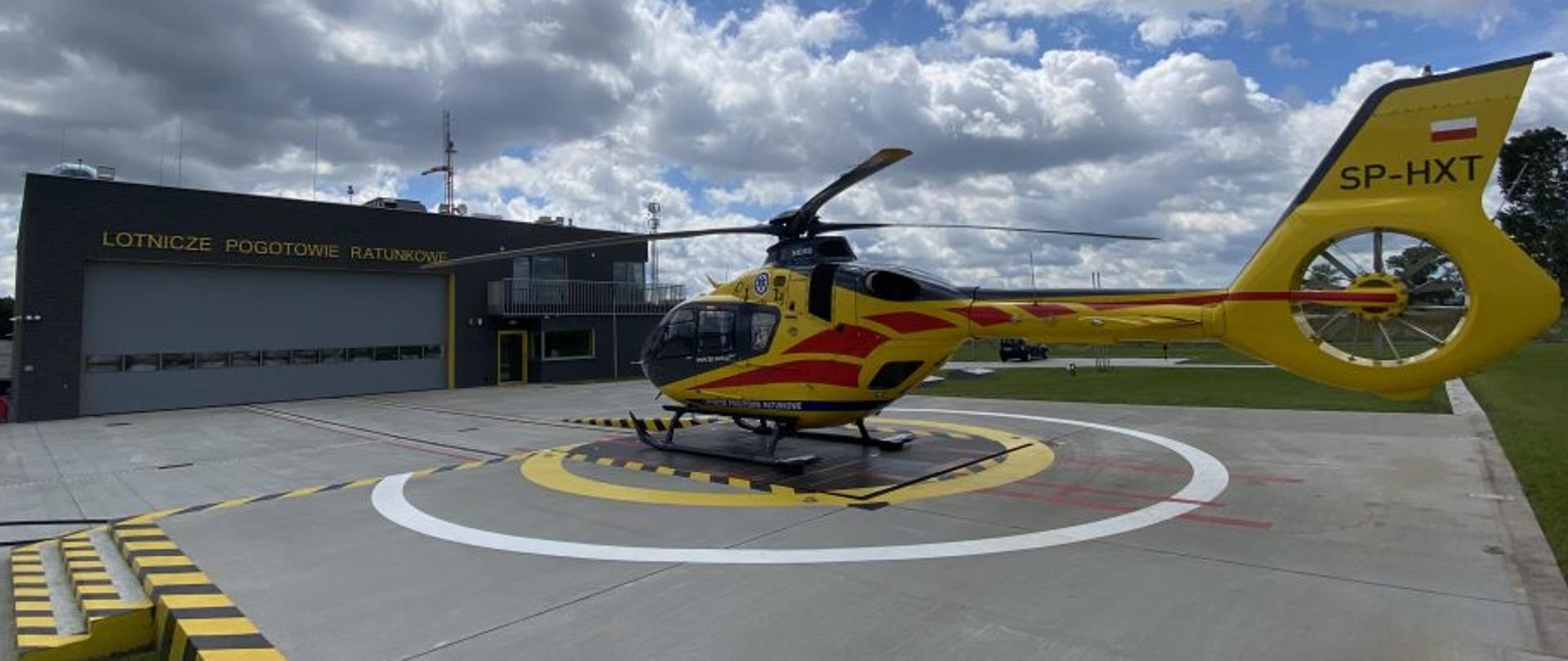 Na zdjęciu śmigłowiec lotniczego pogotowia ratunkowego na tle budynku lotniczego pogotowia ratunkowego