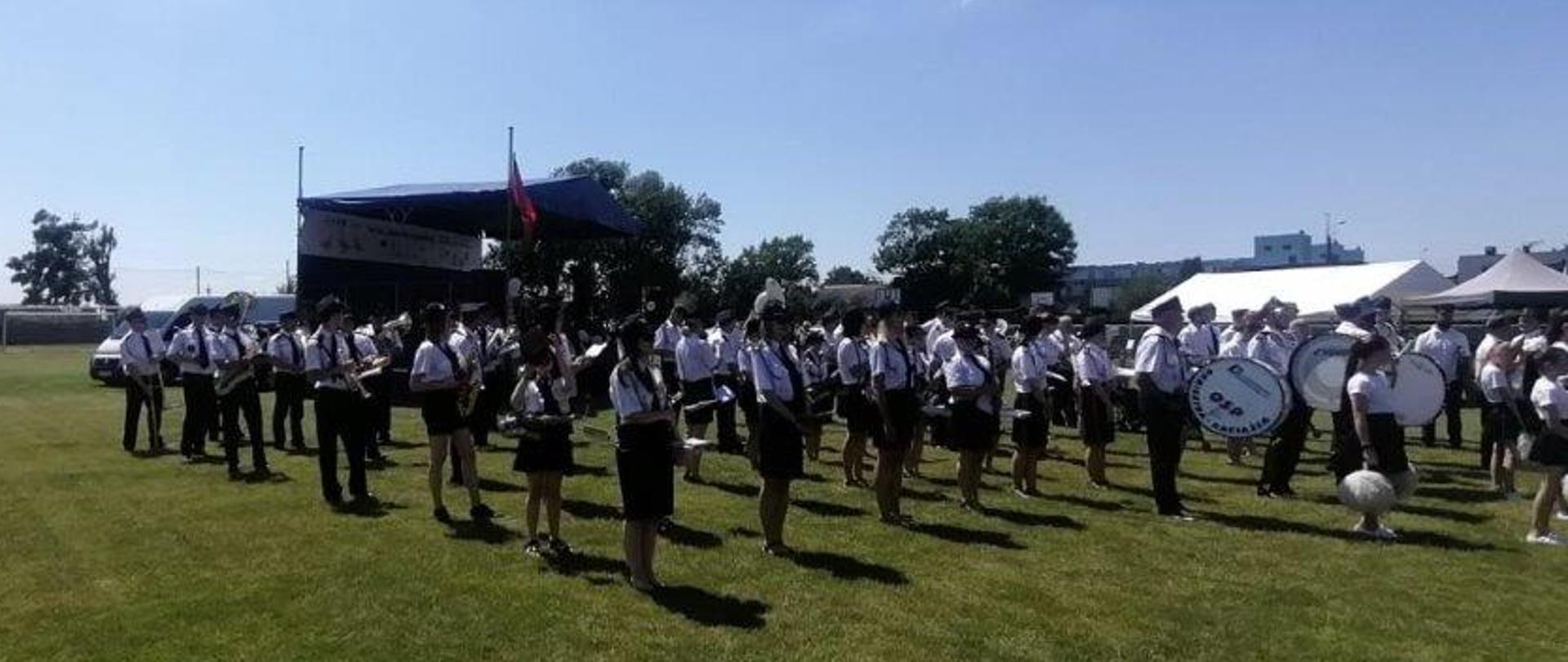 Zdjęcie przedstawia członków Orkiestry Dętej OSP w Raciążku stojących wraz z instrumentami na murawie boiska