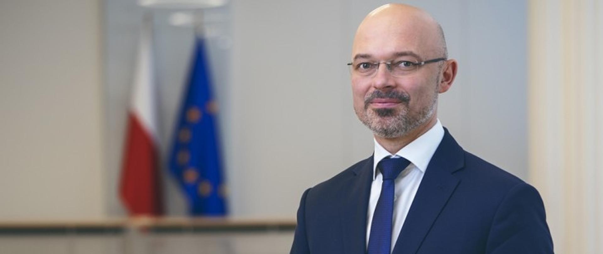 Na zdjęciu widoczny minister Michał Kurtyka a obok niego widać flagi polską i unijną