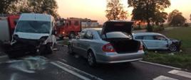 Wieczór, zachodzące słońce, na skrzyżowaniu dróg stoją dwa uszkodzone samochody (jeden dostawczy), w pobliskim rowie stoi trzecie uszkodzone auto. 