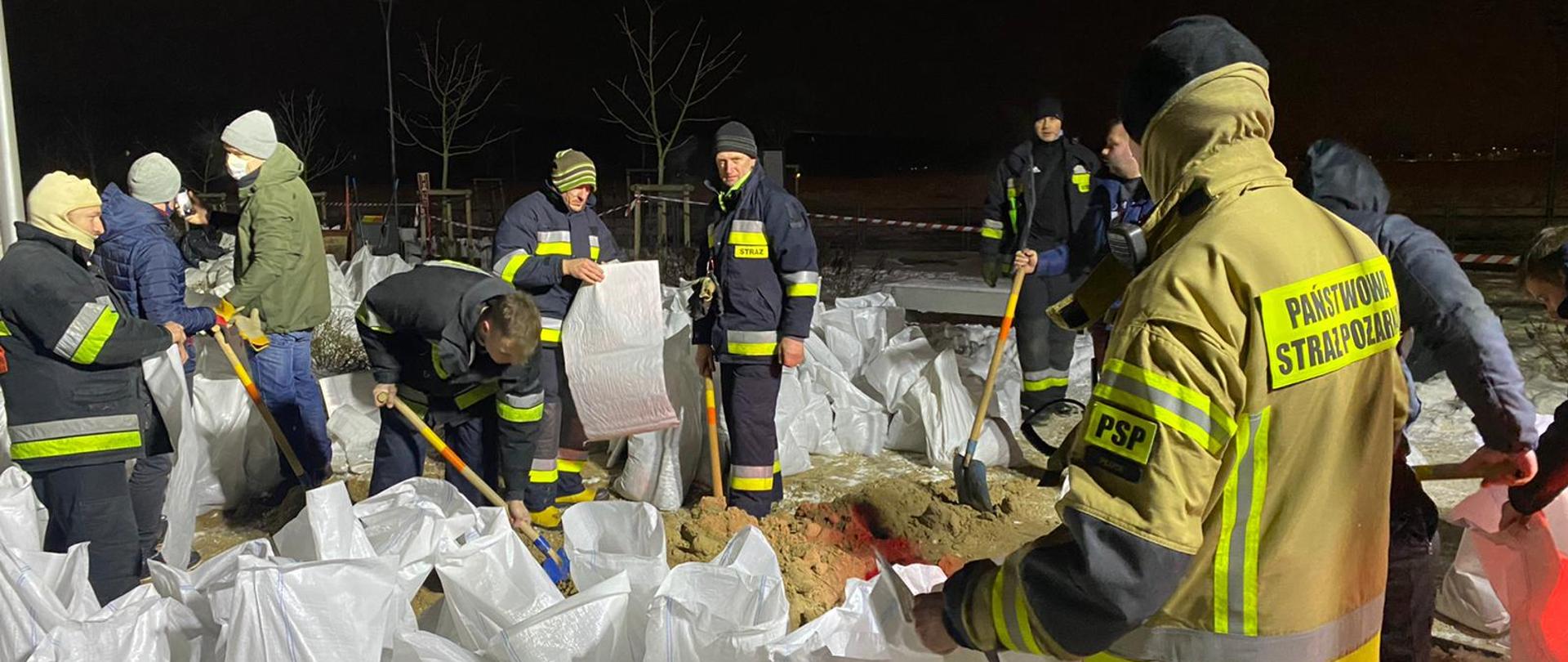 Strażacy napełniający worki z piaskiem. Pora nocna
