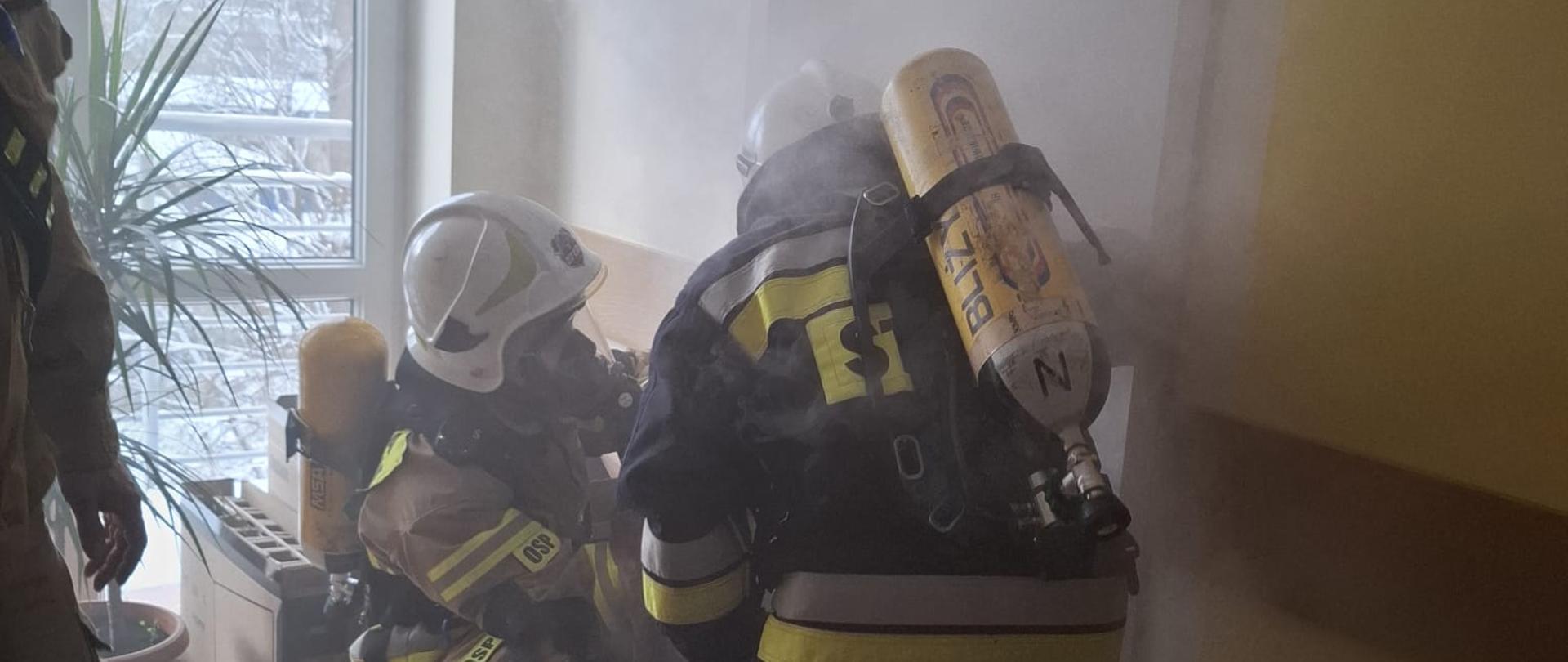 Strażacy OSP wchodzą do zadymionego pomieszczenia budynku DPS celem przeprowadzenia ewakuacji.