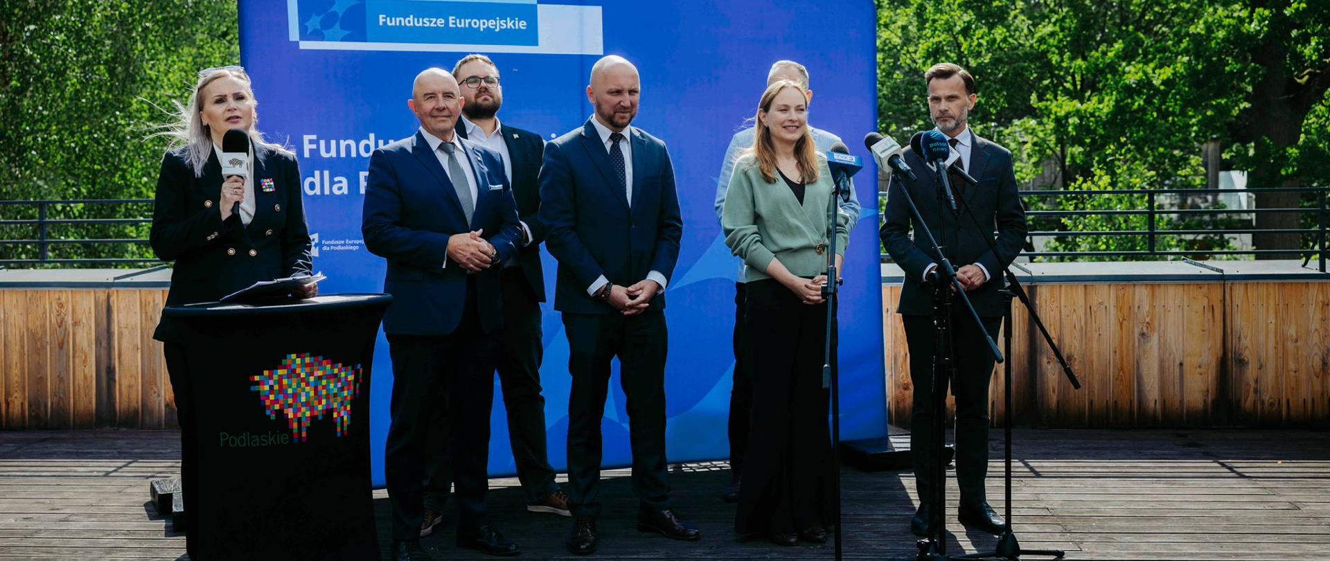 Grupa osób stoi na tle ścianki Fundusze Europejski. Wśród nich minister Katarzyna Pełczyńska-Nałęcz. Przed nimi mikrofony na statywach.