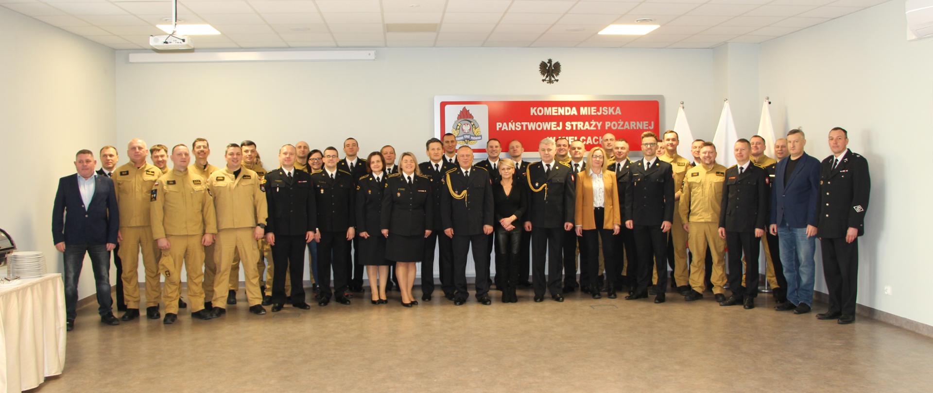 Pamiątkowe zdjęcie: funkcjonariusze i pracownicy Komendy Miejskiej Państwowej Straży Pożarnej w Kielcach. W pierwszym rzędzie stoją w centralnym punkcie odchodzący na emeryturę strażacy.