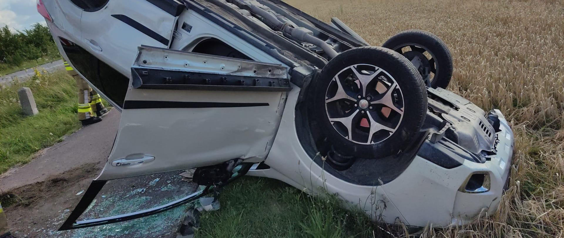 Na zdjęciu widać samochód koloru srebrnego, który leży na dachu. Ma rozbite szyby w drzwiach. 