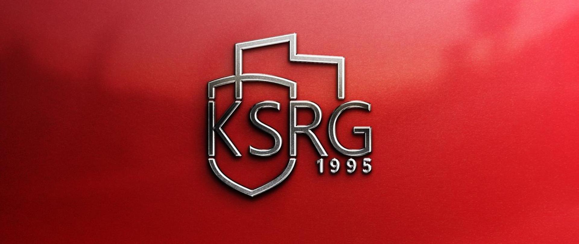 Logo to powstało przez połączenie grafik przedstawiających zarys terytorium Polski oraz tarczę. Pośrodku napis KSRG a poniżej rok powstania 1995. Całość na czerwonym tle.