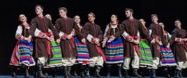 Na scenie tańczy grupa taneczna, ubrani są w regionalne stroje ludowe.