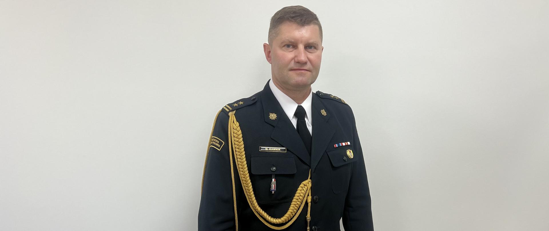 Zdjęcie przedstawia komendanta powiatowego PSP w Tomaszowie Mazowieckim ubranego w mundur galowy ze złotym sznurem. 