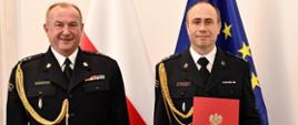 Pomorski Komendant Wojewódzki PSP st. bryg. Jacek Niewęgłowski i Zastępca Komendanta Powiatowego Państwowej Straży Pożarnej w Człuchowie bryg. Marcin Owczarski stoją na tle flagi państwowej i flagi unii europejskiej.