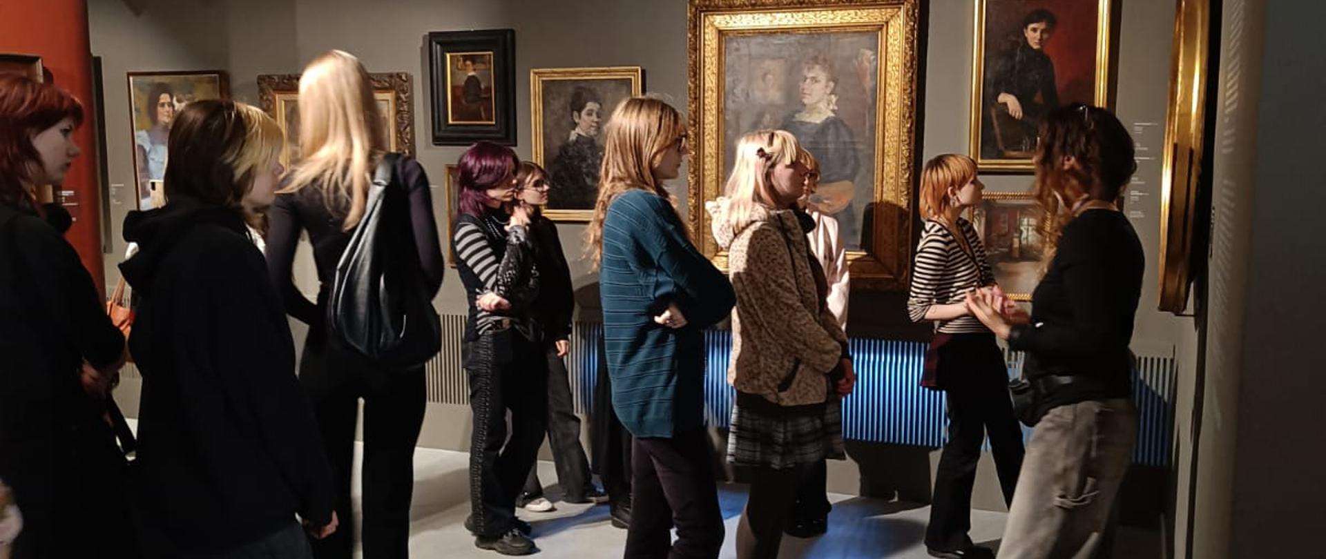 Zdjęcie przedstawia młodzież oglądającą obrazy w muzeum