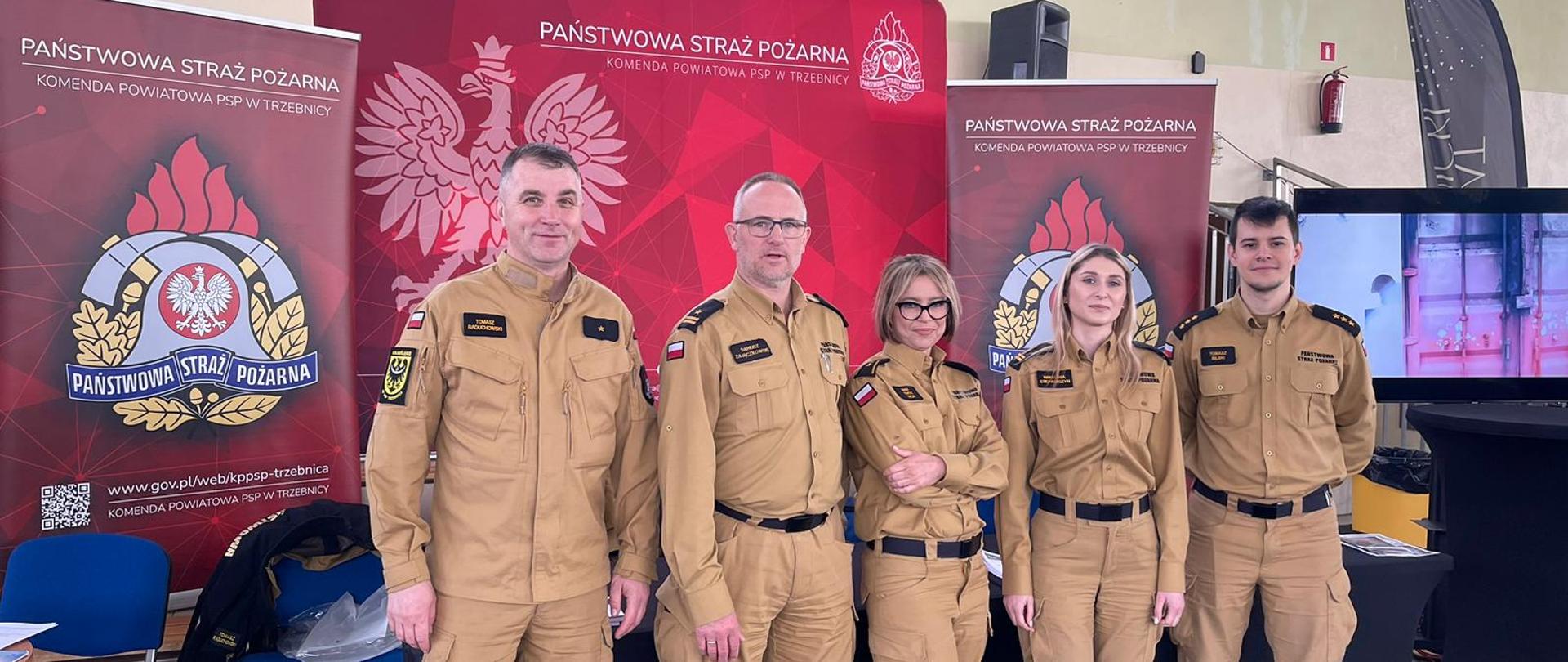 Strażacy na tle banerów promujących straż pożarną