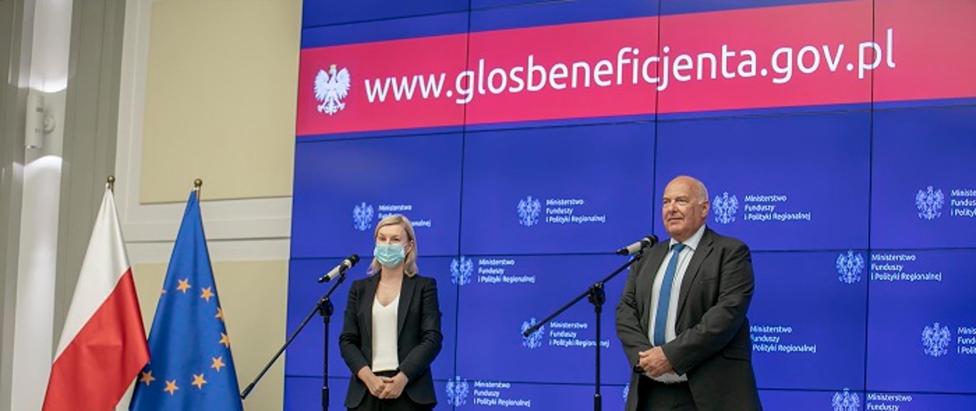 Na scenie stoją minister Tadeusz Kościński oraz rzecznik FE Agata Zielińska. Za ich plecami wyświetla się logo MFiPR oraz napis www.glosbeneficjenta.gov.pl.