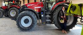Uczestniczka seminarium EUROPEA stoi w hali maszyn rolniczych obok dużego czerwonego ciągnika Case IH. W tle widoczne są kolejne nowoczesne maszyny rolnicze.