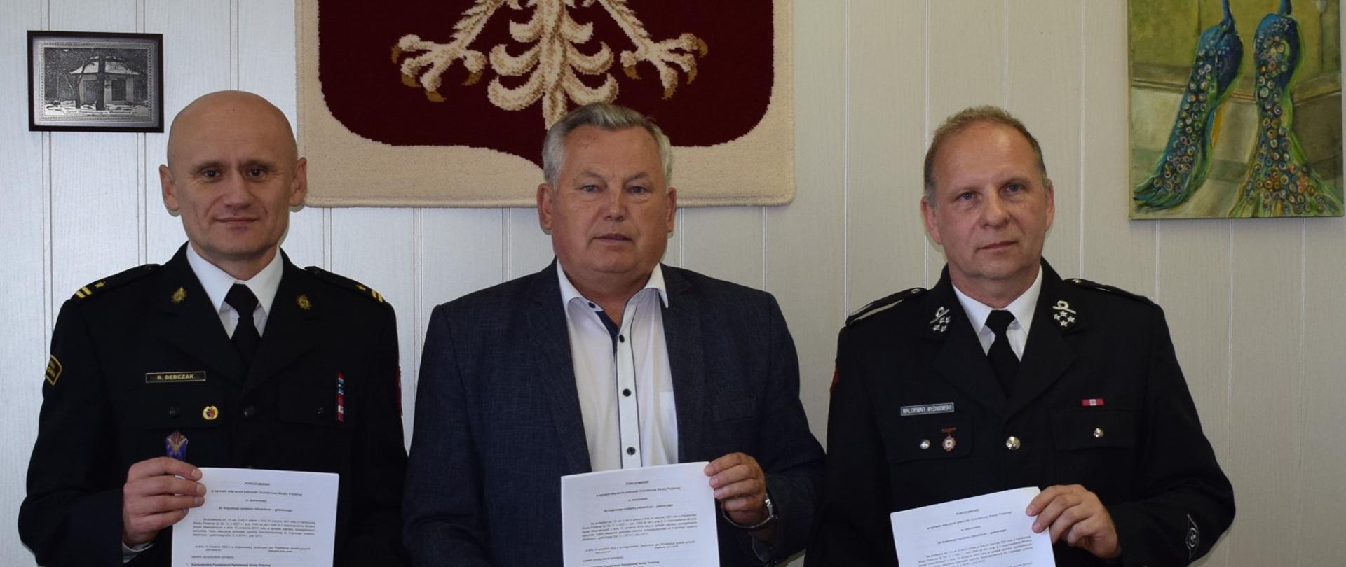 Komendant Powiatowy, Wójt i Prezes OSP trzymają porozumienia. W tle godło Polski