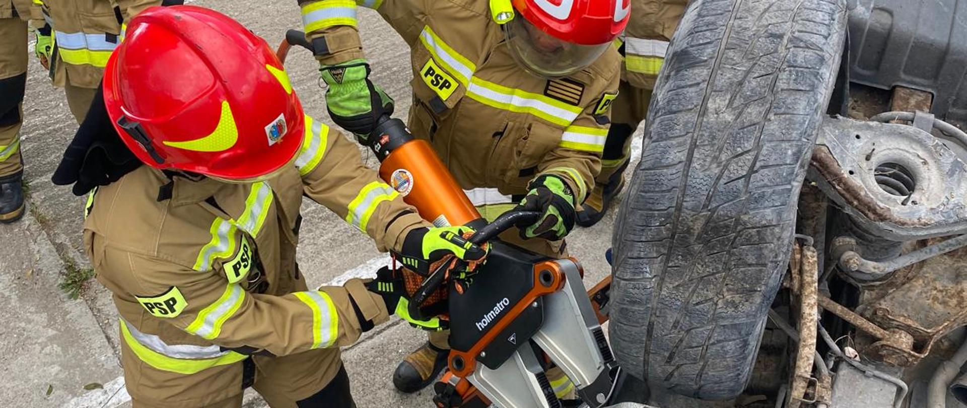 Strażacy PSP podczas ćwiczeń: użycie narzędzia hydraulicznego przy wraku przewróconego samochodu
