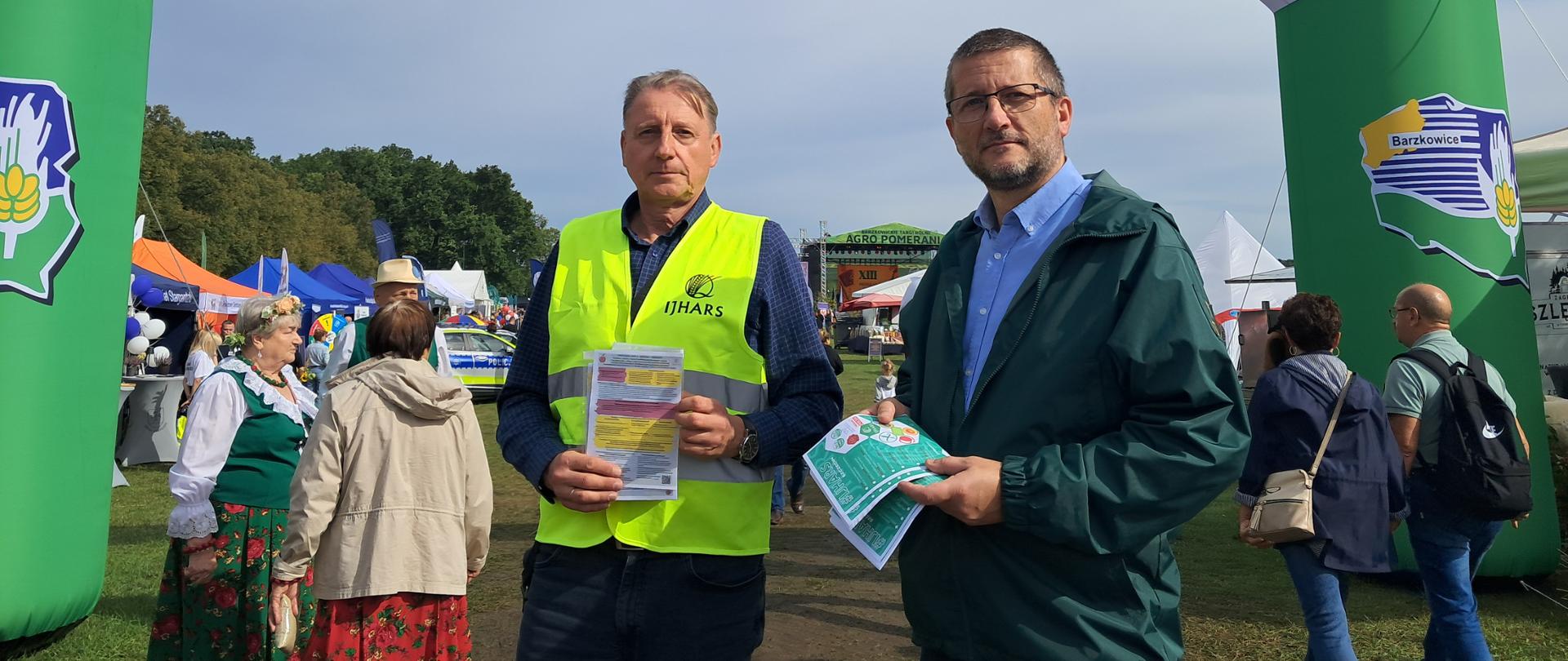 Dwóch inspektorów IJHARS stoi na targach w Barzkowicach, w tle widoczne stoiska wystawców.