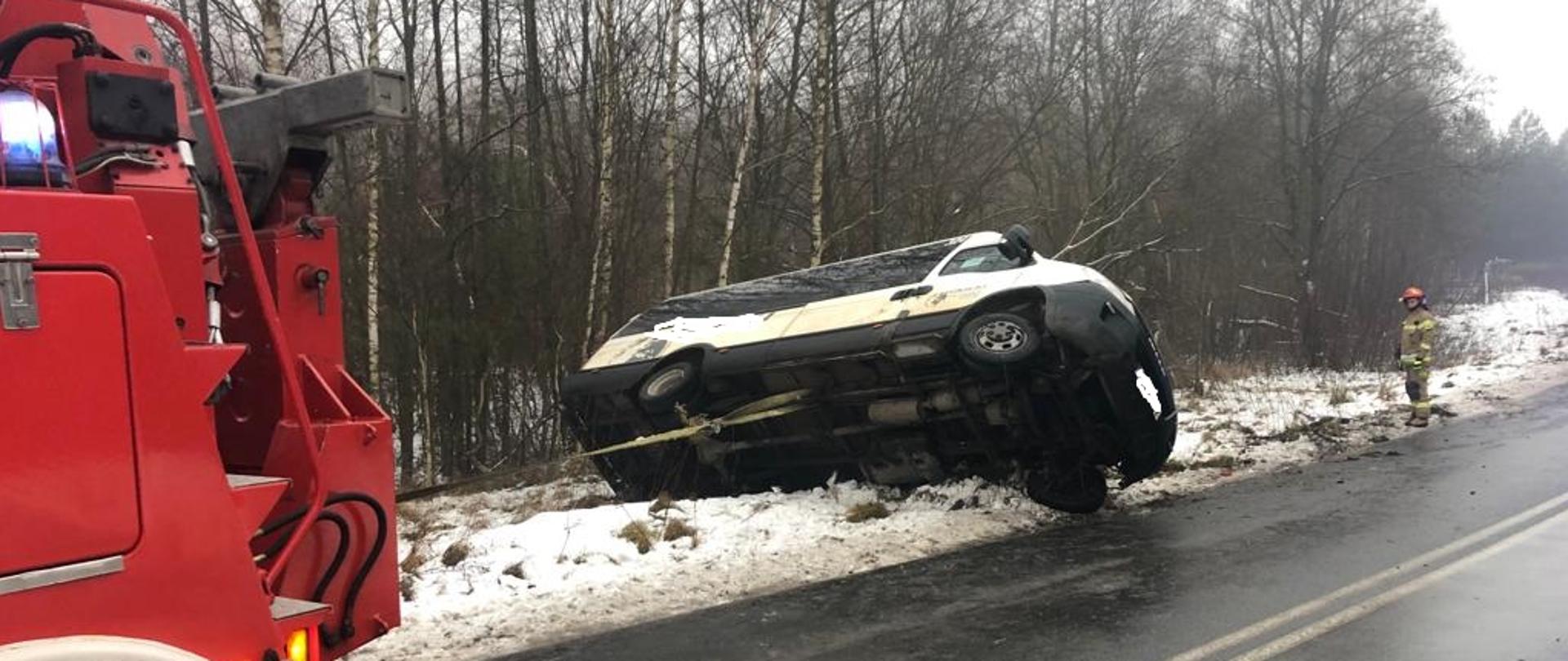 Strażacy przy pomocy specjalnego ciężkiego samochodu ratownictwa technicznego stawiają na koła przewrócony autobus.