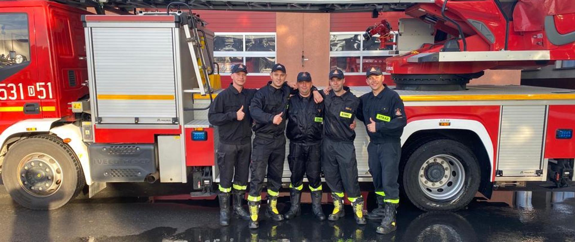 Pięciu strażaków PSP na tle drabiny pożarniczej w śród nich strażak odchodzący na zaopatrzenie emerytalne 