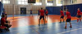 Strażacy ubrani w stroje sportowe grają mecz siatkówki na hali sportowej