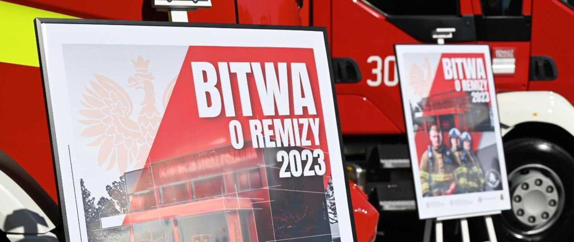 Na zdjęciu widoczny plakat na którym znajduje się samochód pożarniczy koloru czerwonego oraz sztaluga a na nim plakat ze strażakami i samochodem pożarniczym z napisem Bitwa o remizy 2023.