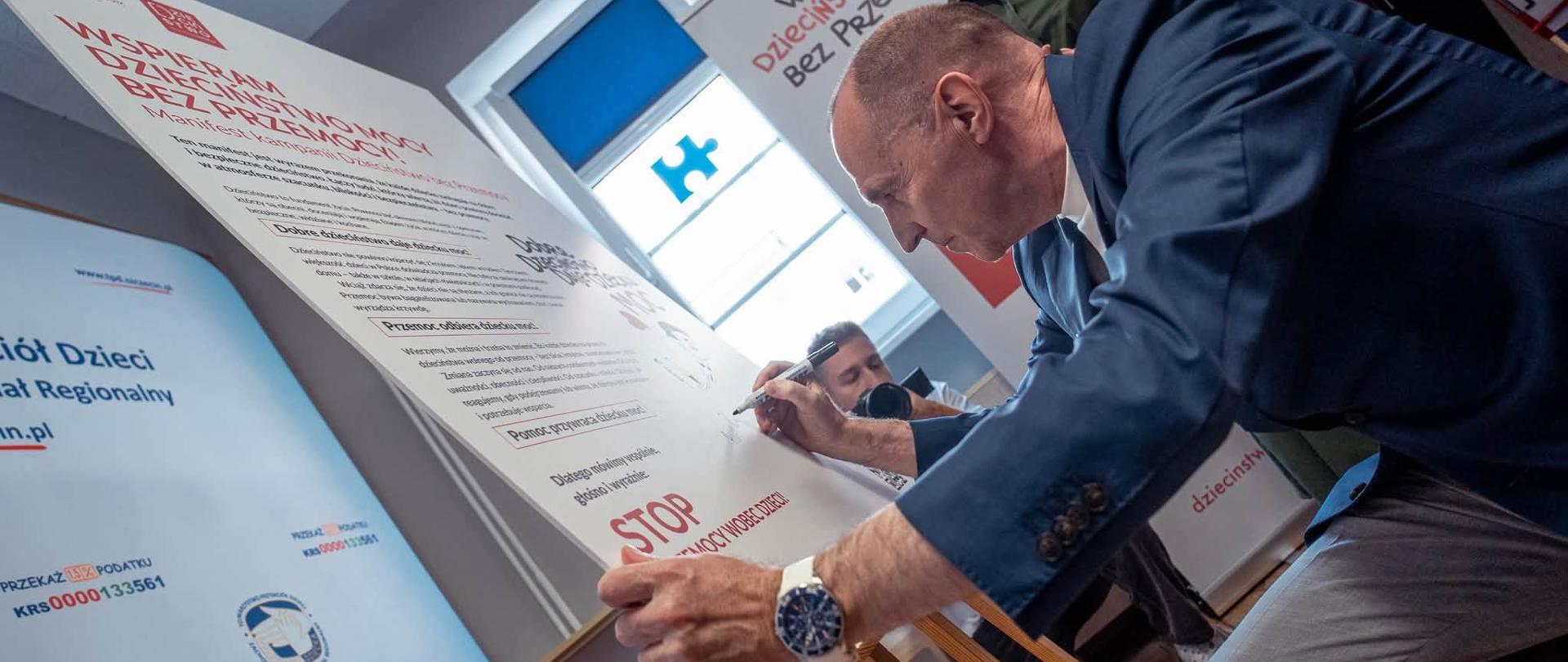 wojewoda podpisuje plakat promujący akcję - Wspieram dzieciństwo bez przemocy