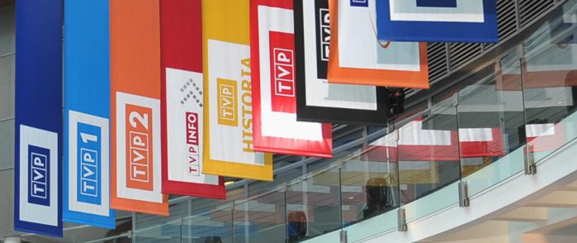 Wiszące w holu głównym TVP chorągwie z logiem programów.