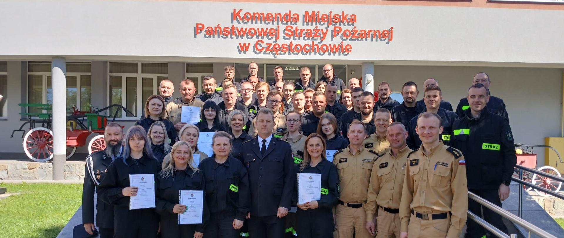 na zdjęciu przed budynkiem Komendy Miejskiej Państwowej Straży Pożarnej w Częstochowie ustawiona grupa absolwentów szkolenia podstawowego wraz Komendantem Miejskim Państwowej Straży Pożarnej w Częstochowie oraz funkcjonariuszami wchodzącymi w skład komisji egzaminacyjnej 