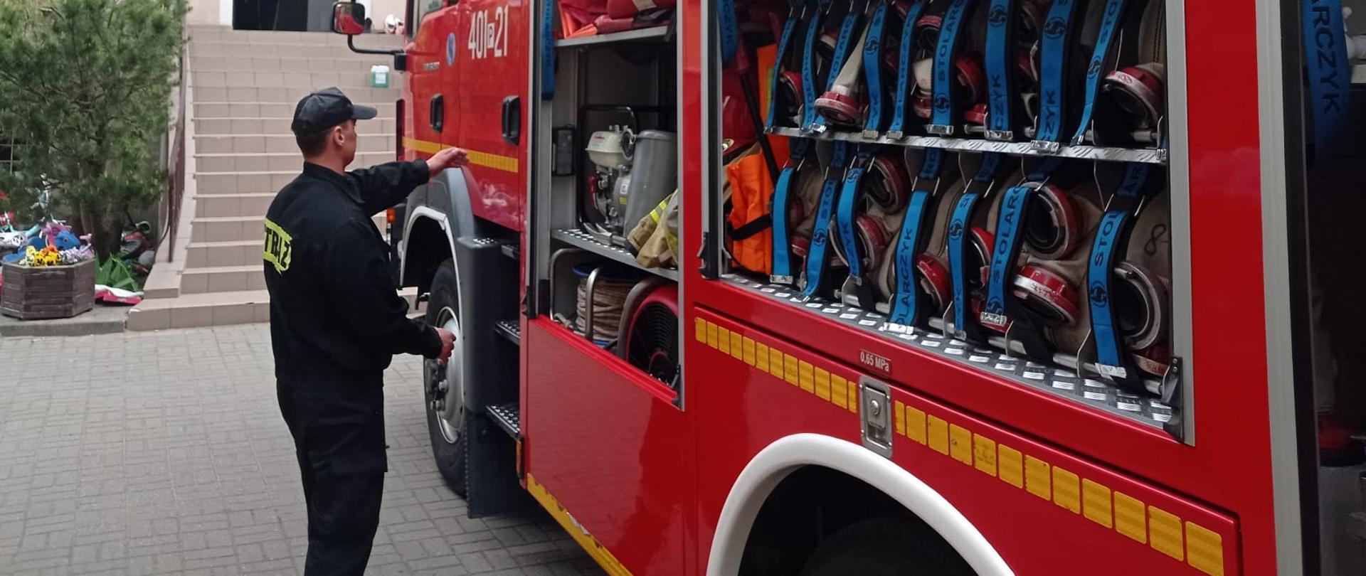 Zdjęcie przedstawia strażaków oraz sprzęt i pojazdy strażackie podczas rozpoznania operacyjnego obiektu.
W tle budynek.
