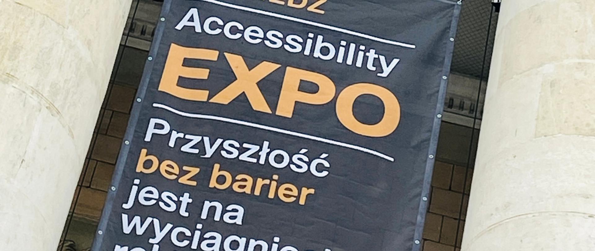 Fragment fasady pałacu kultury i nauki w Warszawie, pomiędzy dwoma kolumnami z głowicami kompozytowymi rozpięty jest Baner z napisem: odwiedzić Accessibility Expo – przyszłość bez barier jest na wyciągnięcie ręki