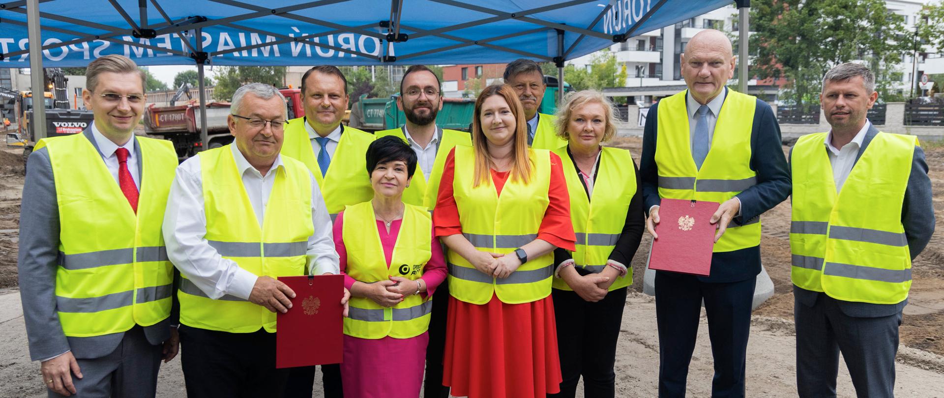 
Grupa osób w żółtych kamizelkach na placu budowy

