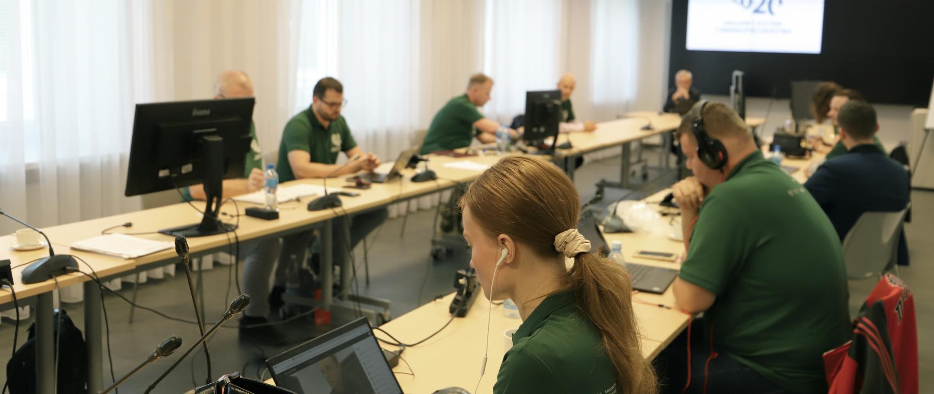 Uczestnicy szkolenia siedzą wokół stołu - w słuchawkach, patrzą w komputery. 