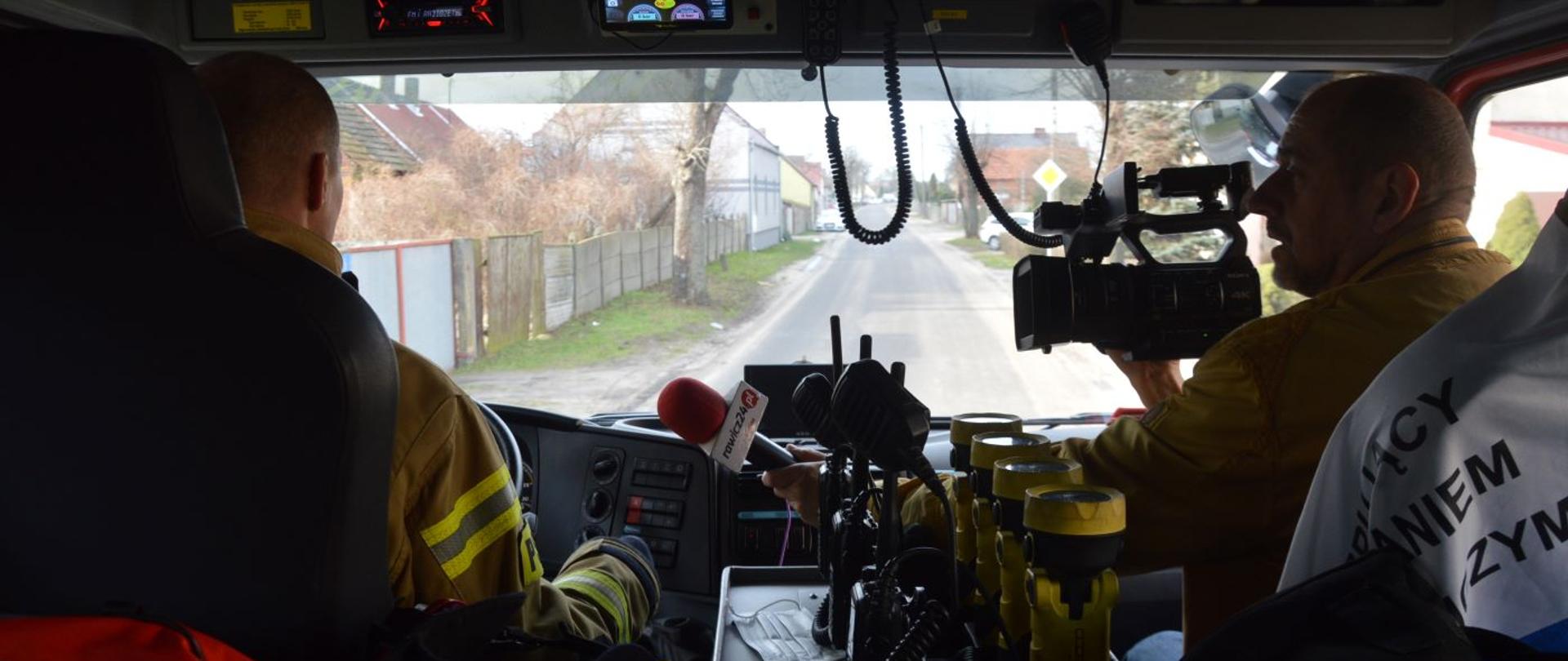 Przygotowywanie spotu edukacyjnego. Jedna z ulic w Dębnie Polskim. Wnętrze wozu strażackiego. Kamerzysta wykonuje zdjęcia w trakcie jazdy. Siedzi na miejscu dowódcy i nagrywa wypowiedź kierowcy wozu.