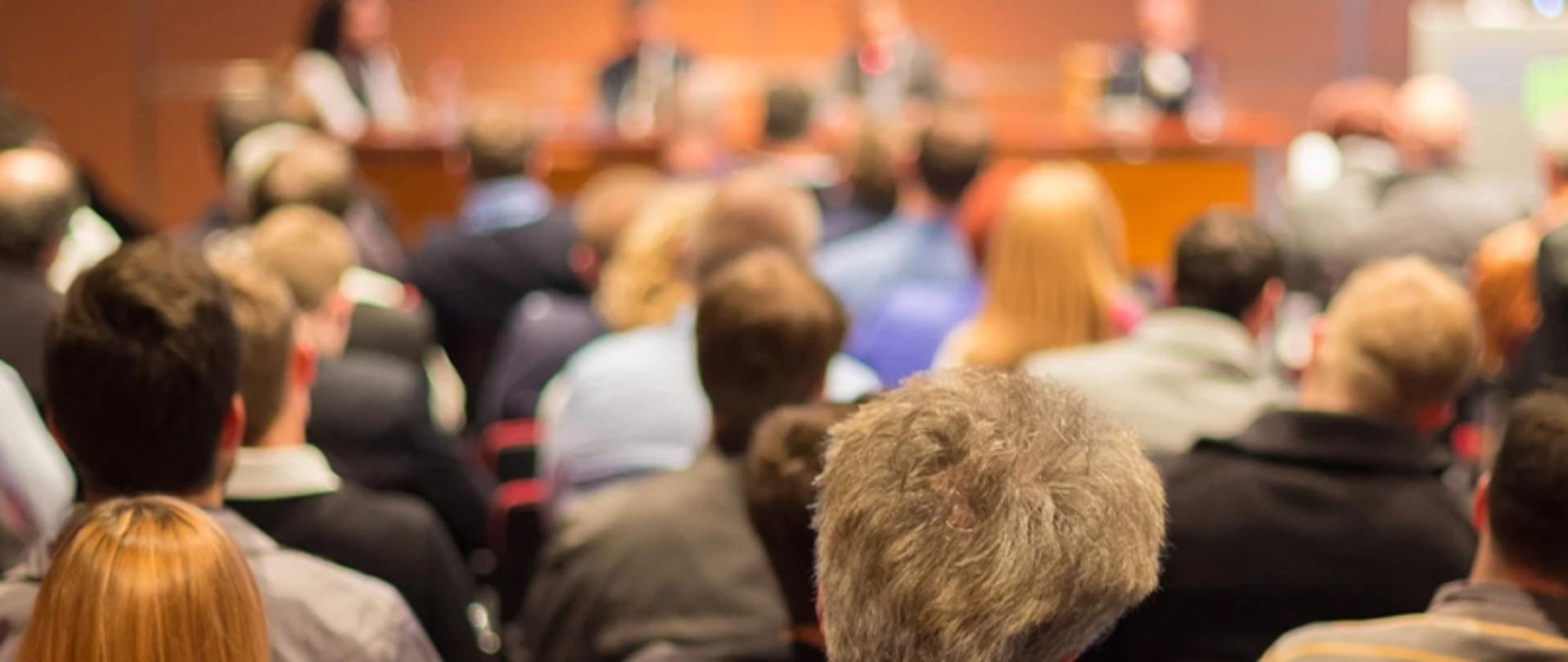 Uczestnicy konferencji lub szkolenia siedzący na sali i słuchający prelegentów przy stole panelowym — wydarzenie związane ze współpracą edukacyjną ze środowiskiem inżynierów budowlanych.