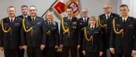 Na zdjęciu widać dziewięciu strażaków w umundurowaniu wyjściowym. W tle sztandar Komendy Głównej PSP. W środku stoi komendant główny PSP.