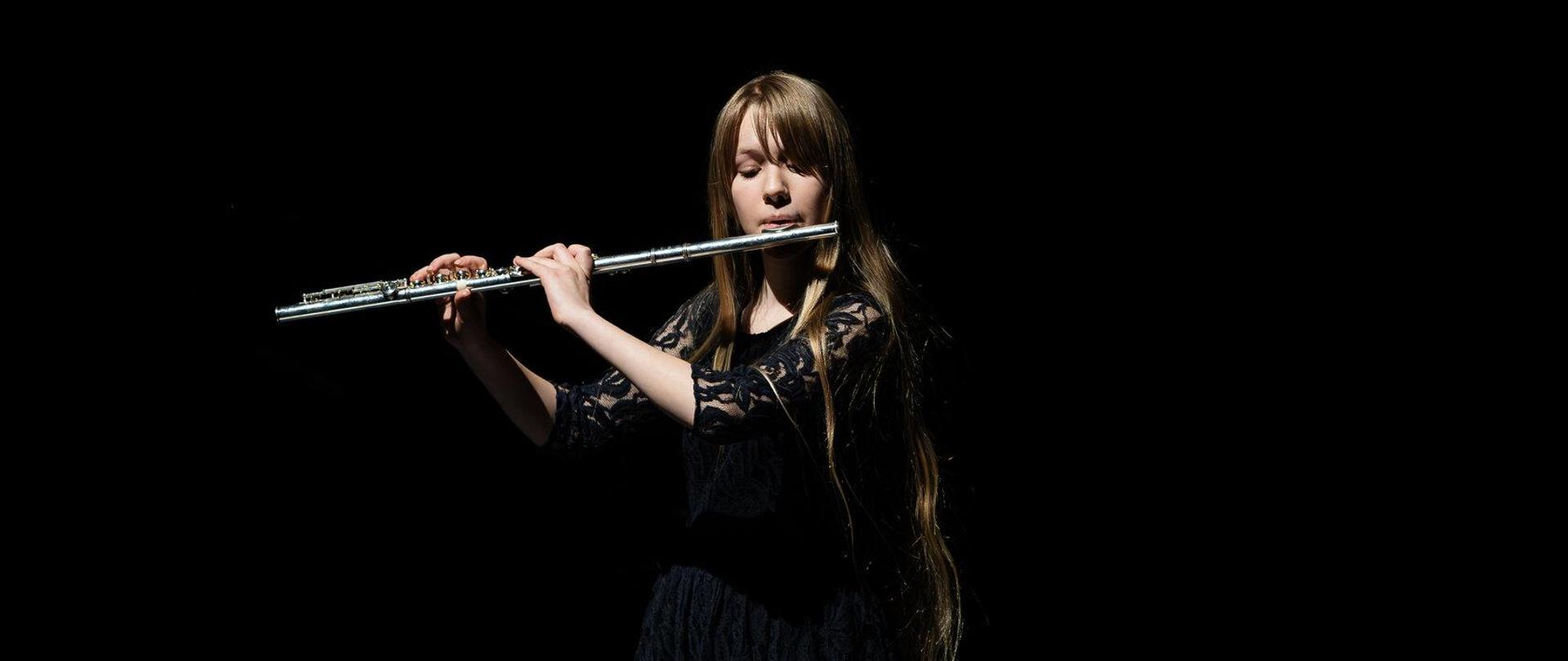 Uczennica gra na flecie na scenie w budynku.