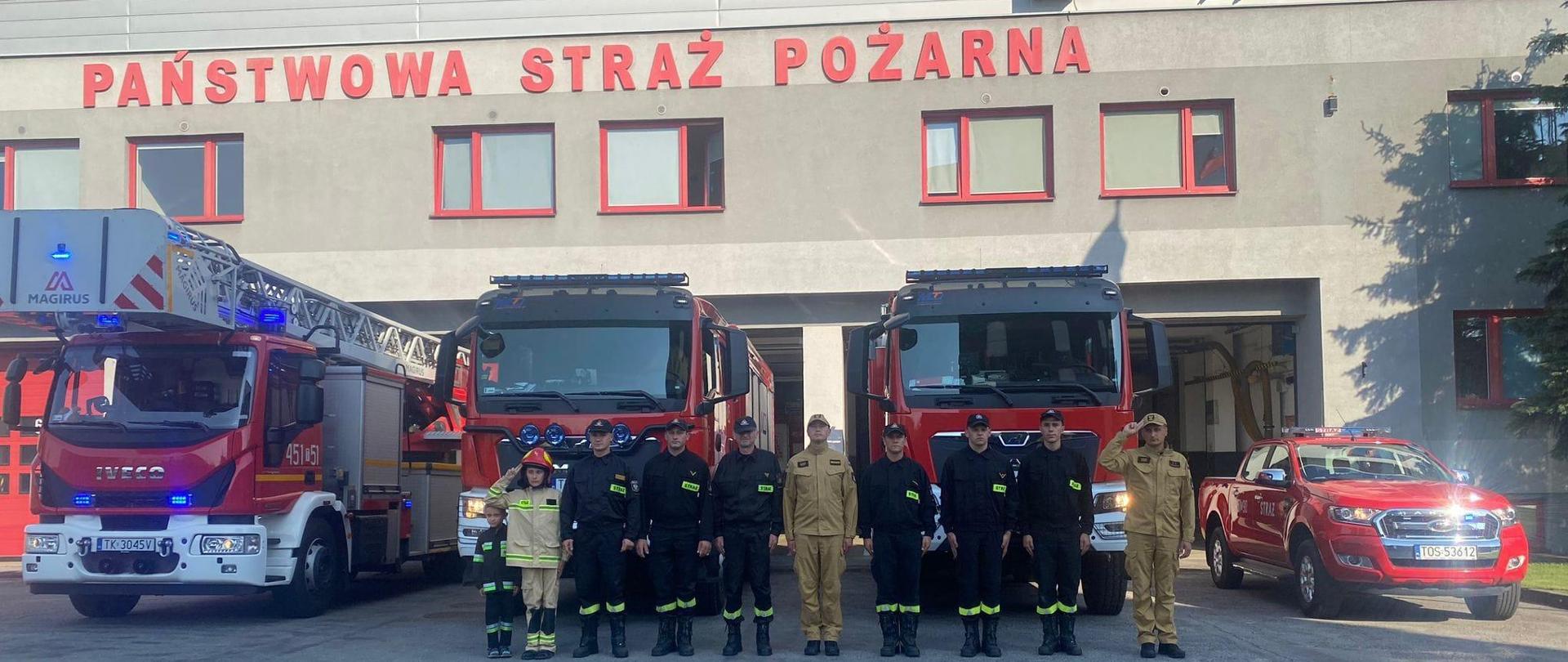 Na zdjęciu widoczni są strażacy na tle samochodów ratowniczo - gaśniczych oddający hołd bohaterom Powstania Warszawskiego