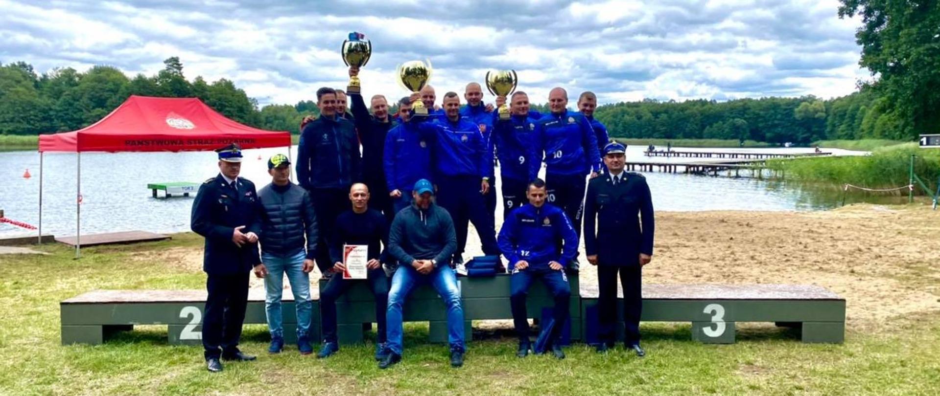 Grupowe zdjęcie zwycięzców zawodów, w tle jezioro i drzewa