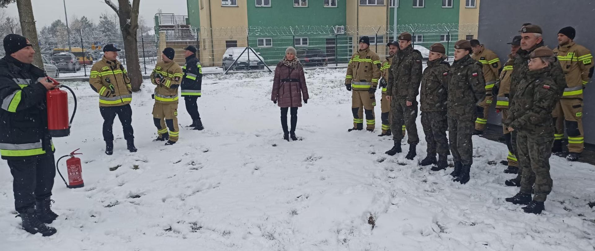 Strażacy i żołnierze słuchają instruktarzu o prawidłowym użyciu gaśnic.