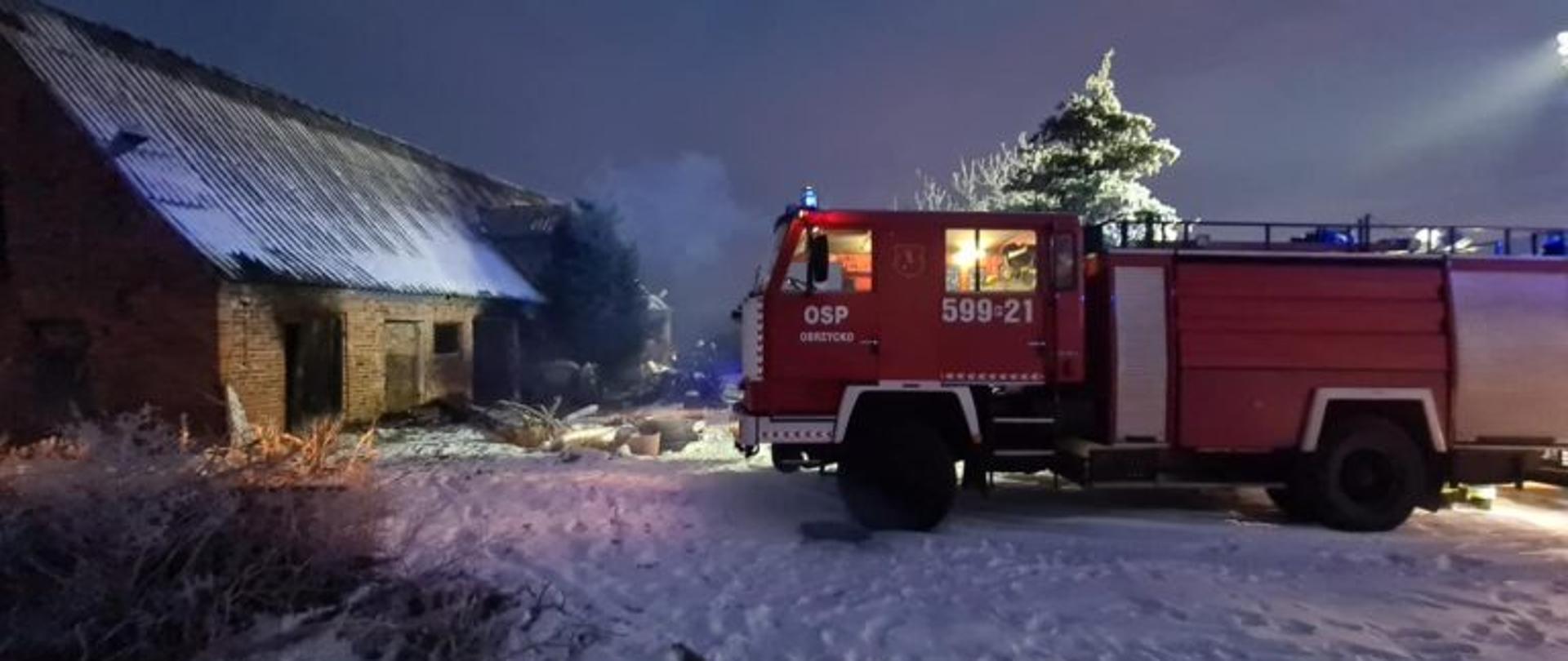 Widać budynek gospodarczy i samochód strażacki